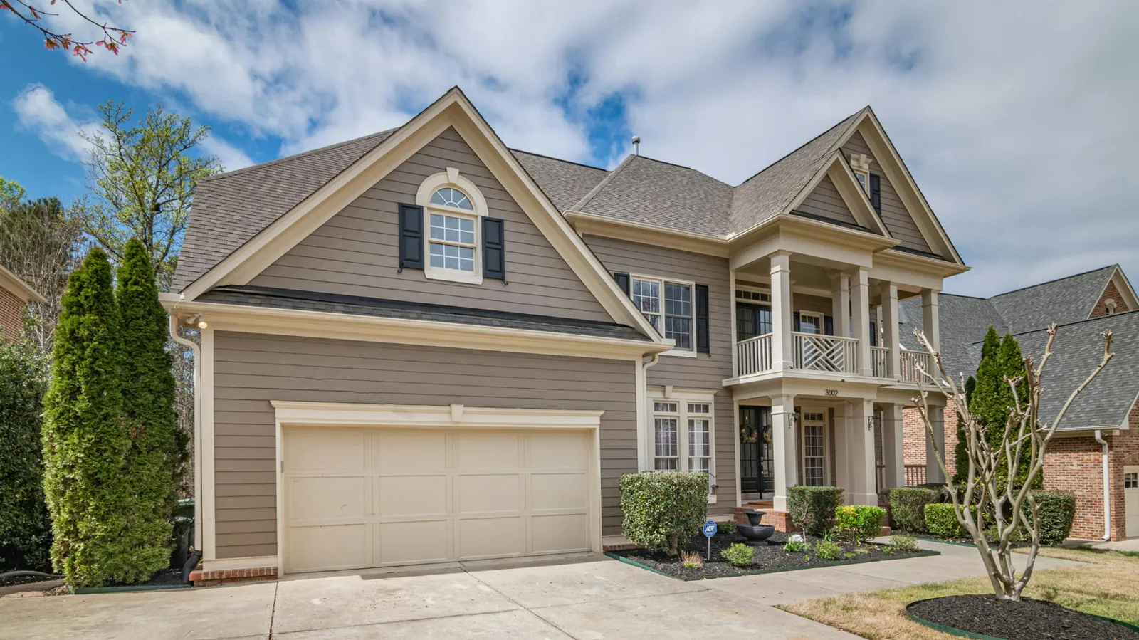 Tan two-story home with a columned balcony and brown asphalt shingle roof