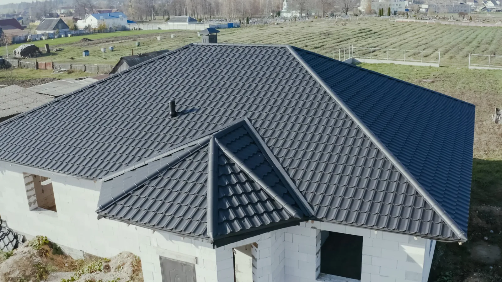 Fields beyond a block house topped with a dark metal tile hip roof