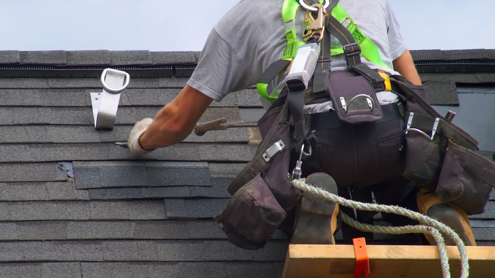 Shingle fitted on a gray roof by a roofer wearing a safety harness