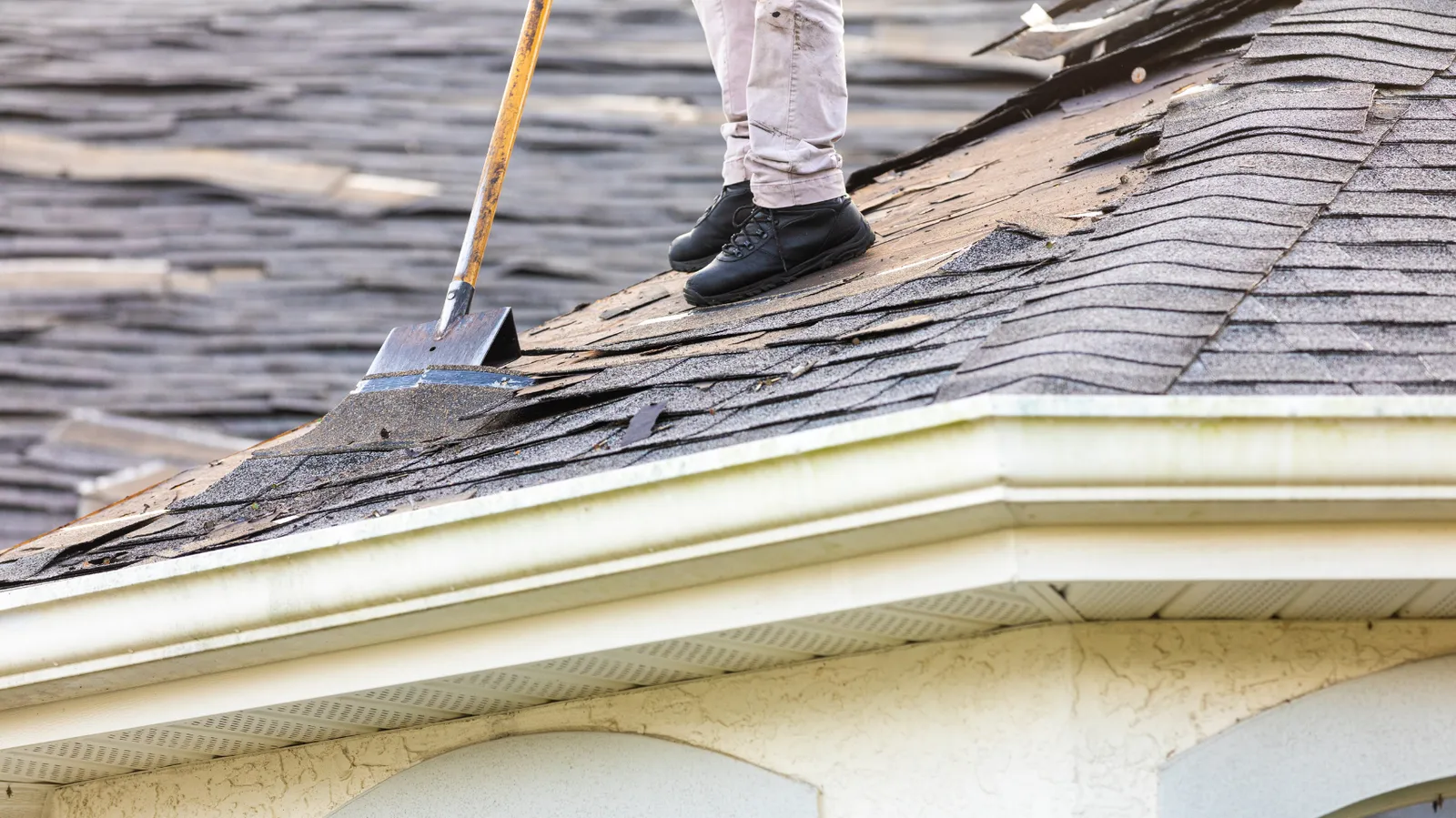 Shovel wedged under shingles as a roofer stands at a roof edge