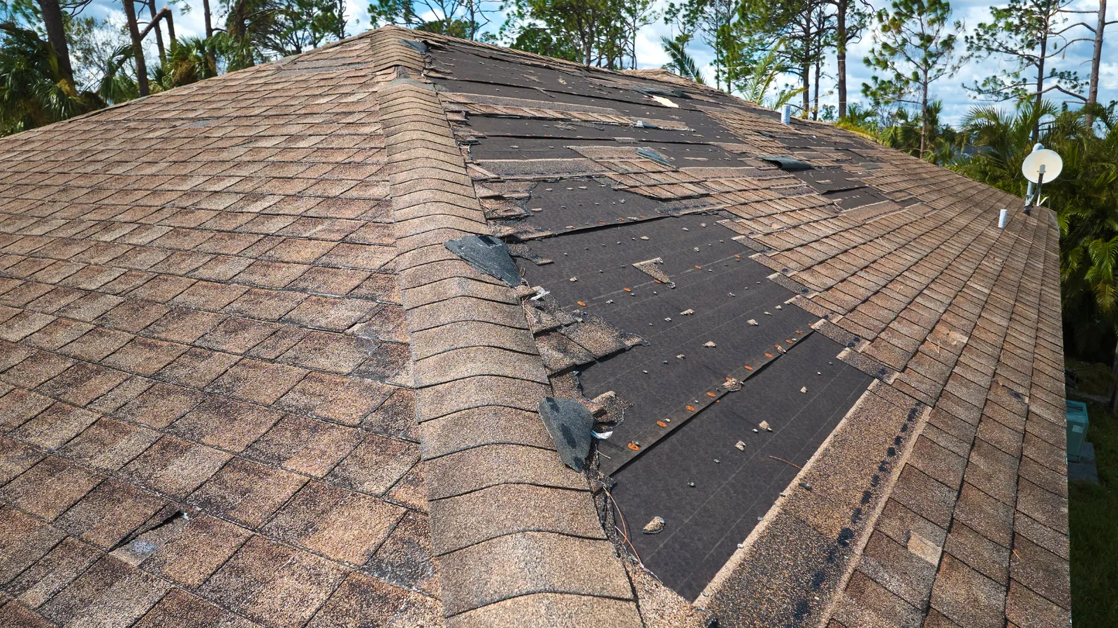 Brown hip roof missing large patches of shingles